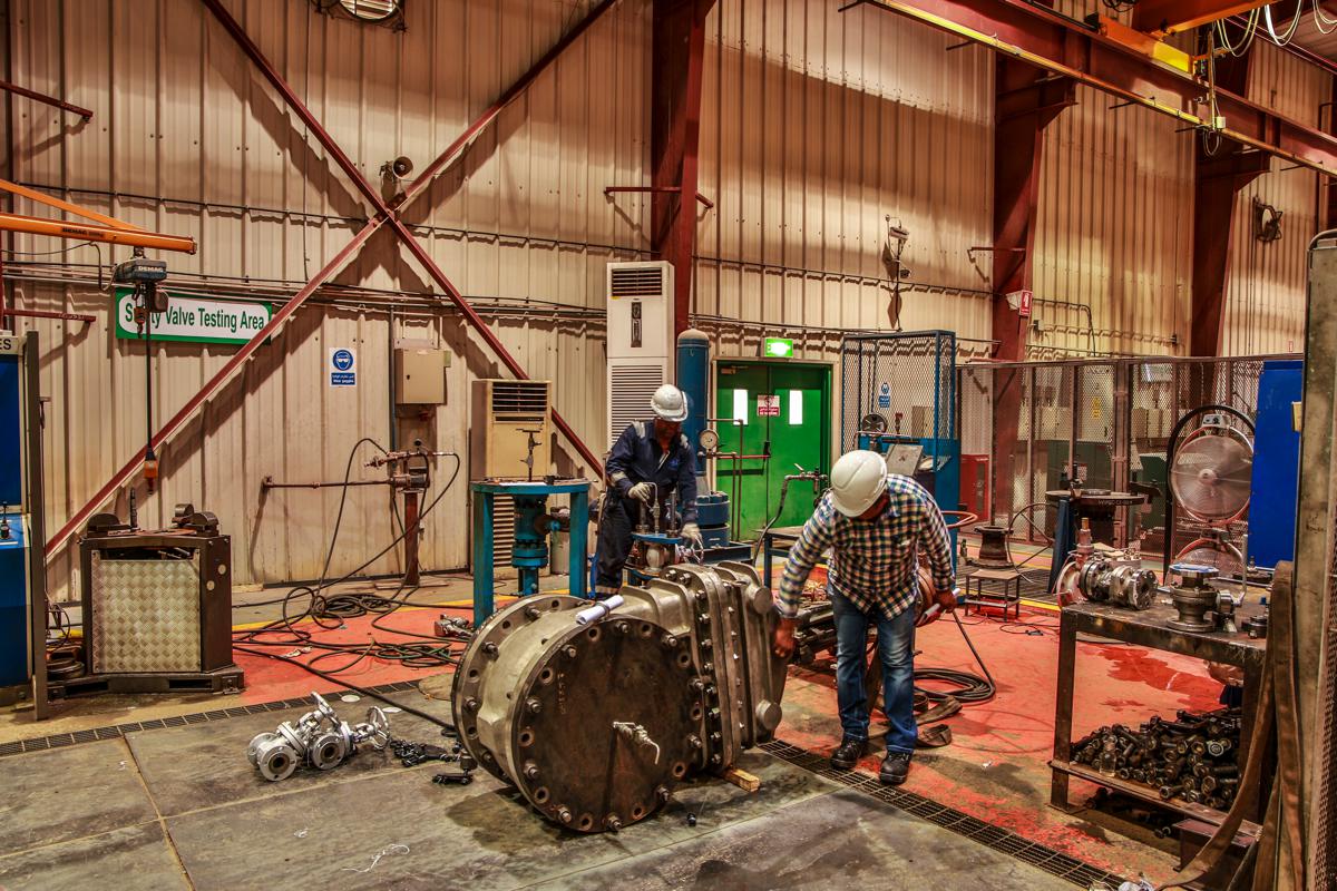 Two technicians working on a large flanged valve body in the safety valve testing area