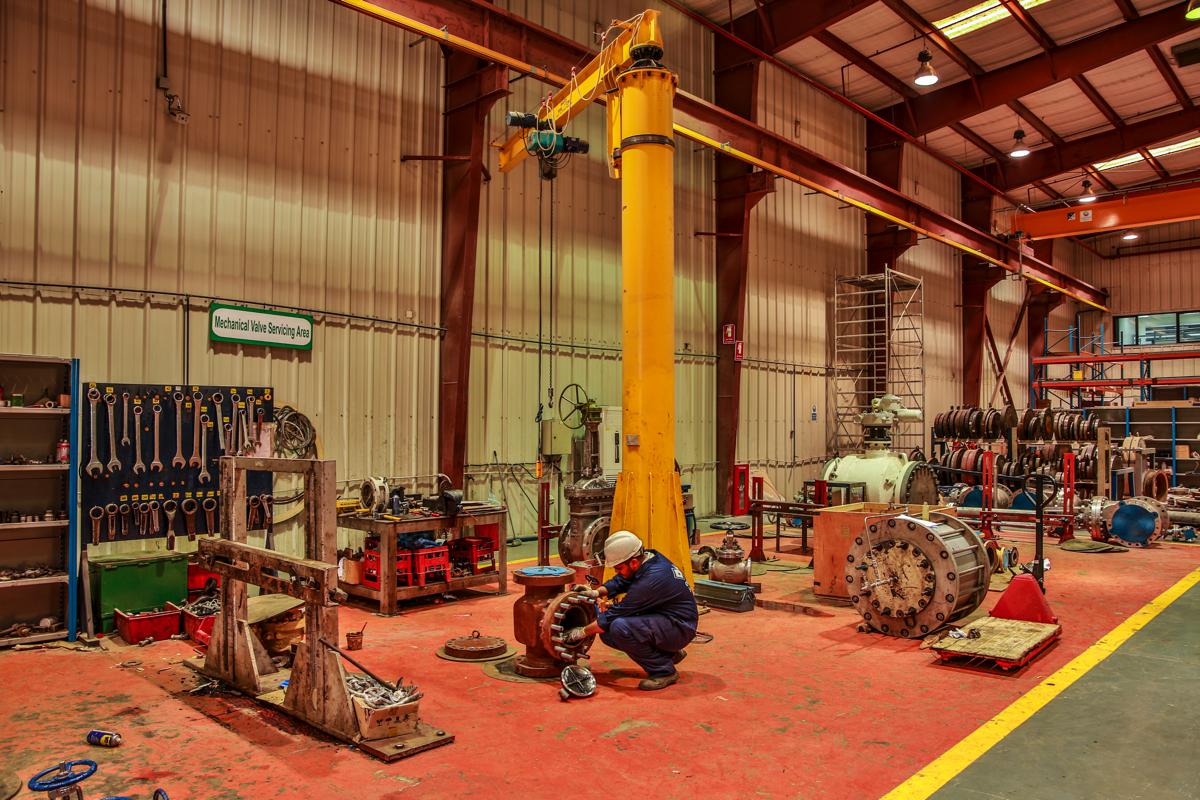 A technician working on a valve beneath a yellow jib crane in the mechanical valve servicing area